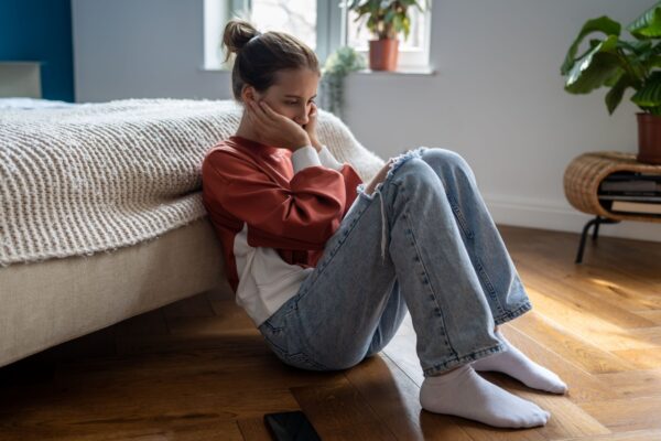 Unhappy depressed teenage girl sitting on floor at home waiting for call from boyfriend, feeling sad and heartbroken after receiving break up text message, cant forget ex. First love, adolescence.