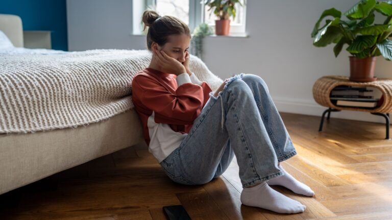 Unhappy depressed teenage girl sitting on floor at home waiting for call from boyfriend, feeling sad and heartbroken after receiving break up text message, cant forget ex. First love, adolescence.