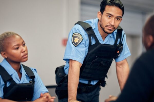 Interrogation, arrest and police team with a suspect for questions as law enforcement officers. Security, crime or investigation with a serious man and woman cop talking to a witness for information