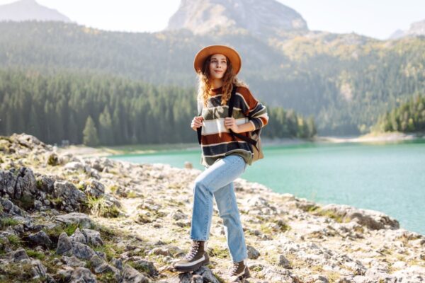 Active woman with backpack solo travel near lake on wooded mountains background. Adventure and travel exploring. Hiking.