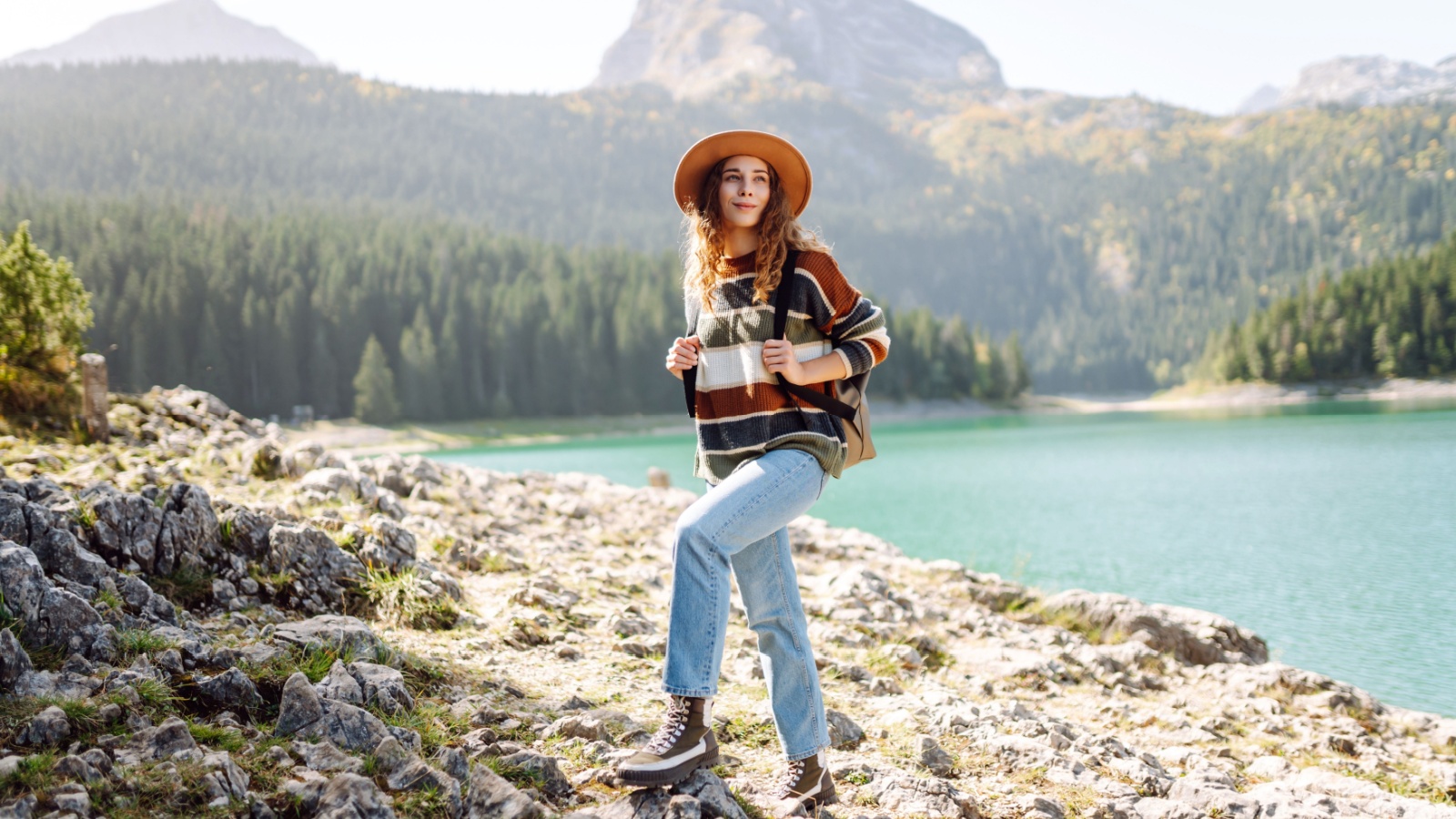 Active woman with backpack solo travel near lake on wooded mountains background. Adventure and travel exploring. Hiking.