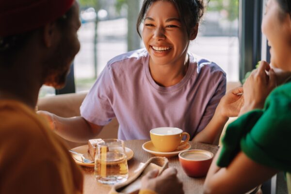 Three multiethnic friends are talking over coffee and cake, laughing and enjoying each other's company in a bright and cozy cafe. Meeting concept