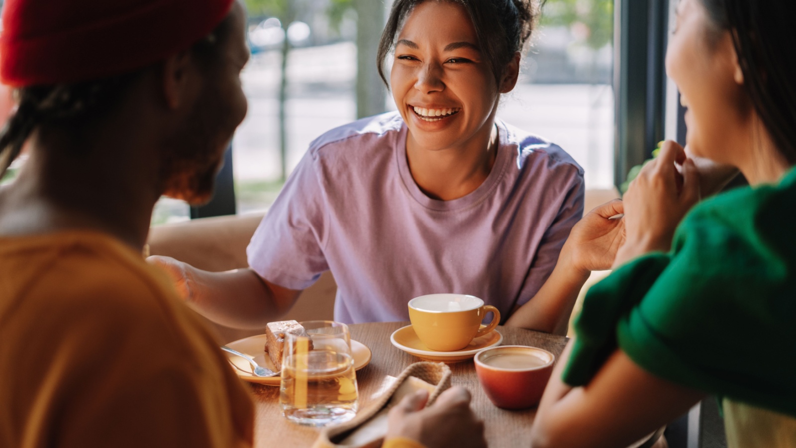 Three multiethnic friends are talking over coffee and cake, laughing and enjoying each other's company in a bright and cozy cafe. Meeting concept