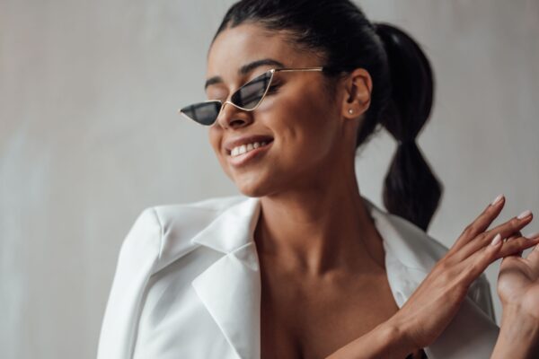 Young adult beauty swarthy woman in formal evening white suit with bra at cat eye sunglasses. Stylish black curly hair sensual african american model fashionista posing at studio in fashion pantsuit