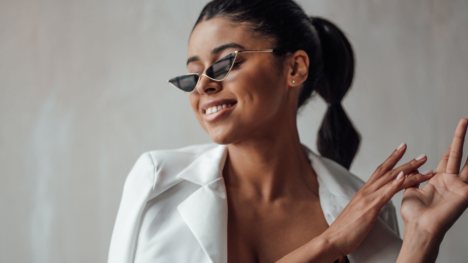 Young adult beauty swarthy woman in formal evening white suit with bra at cat eye sunglasses. Stylish black curly hair sensual african american model fashionista posing at studio in fashion pantsuit