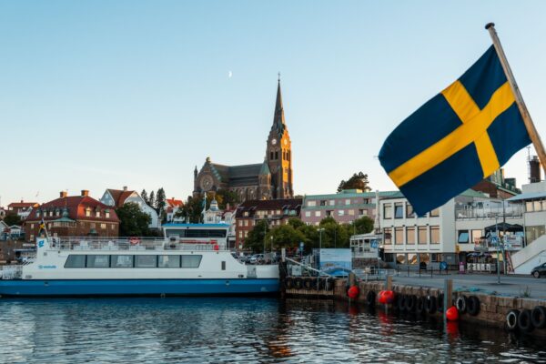 Lysekil, Sweden - July-12-2024, Ferry landing in the port with the church in the backgroundunder the moon in a midsummer night. A Sweden Flag waving in the foreground.