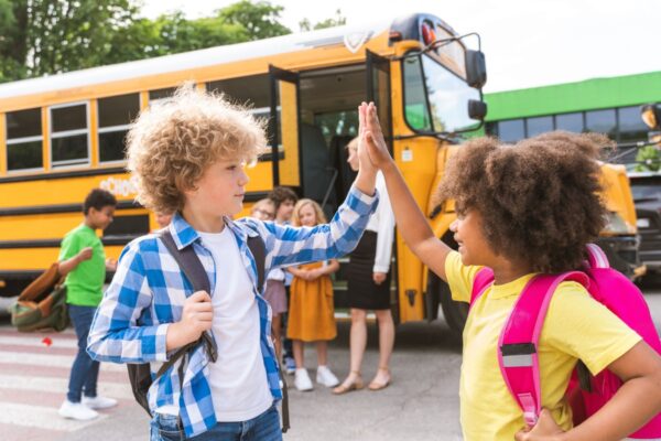 Group of young students driving to primary school on a yellow school bus - Elementary school kids having fun on a school trip