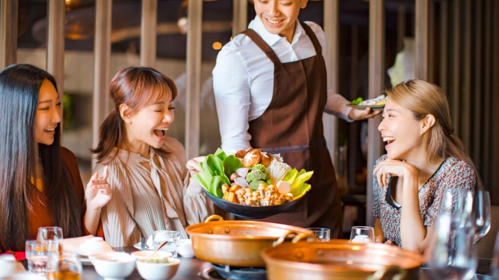 waiter bring vegetables for hot pot and serving group of friends in restaurant