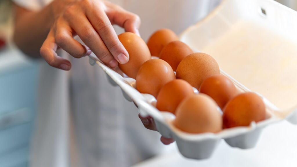 women with holding a cardboard egg box full of her eggs. the girl takes one chicken egg from a white box