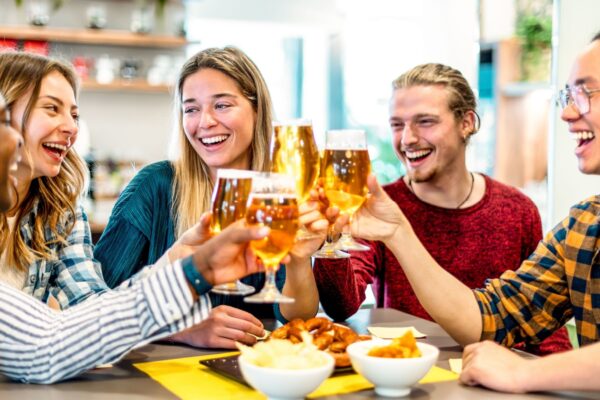 Happy friends drinking beer at brewery bar restaurant on weekend - Friendship concept with young smiling people having fun together toasting brew pint on happy hour at pub - Men and women at home